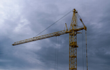Old high-rise construction crane. Yellow color of paint. Gloomy cloudy sky.