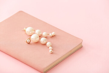 Beautiful earrings with notebook on color background