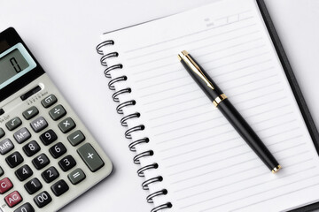Pen, calculator on notebook close up on white background