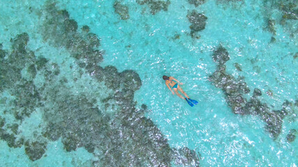 TOP DOWN: Flying above a tourist girl snorkeling around the decaying reef.