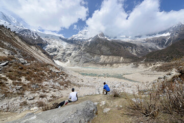 Fototapeta na wymiar Hikers sitting and enjoying a view of an alpine lake high in the Himalayas along the Manaslu Circuit trek in Nepal