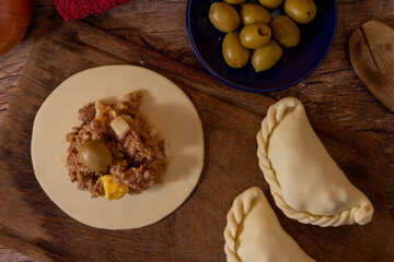 La tradicional empanada de carne argentina, sus ingredientes, carne, huevo, cebolla, aceituna y condimentos tabla de madera rústica