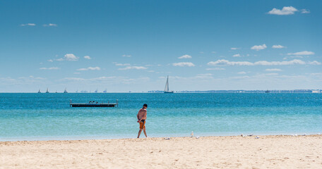 Man walking along the foreshore at Mangles Bay Rockingham with pontoon and yacht in the background