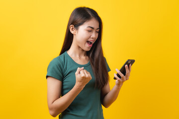 Shocked asian teenager in green tee shirt looking at mobile phone and having shock face on yellow...