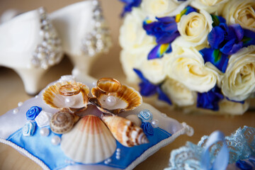 Bridal bouquet, wedding rings on a pillow with shells, bride's shoes, garter. Wedding details in a marine style. The morning of the bride. Marriage preparations