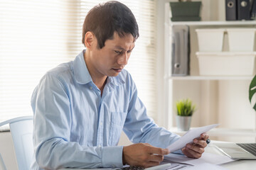 Fototapeta na wymiar Stress Asian man looking at household invoice and credit card bills.