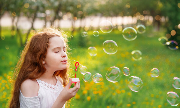 Beautiful girl blowing soap bubbles in summer park.