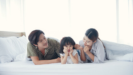 Happy asian young family spend time together. Dad mom daughter are smiling lying on the bed at bedroom