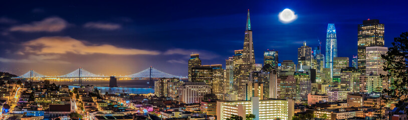 Fototapeta na wymiar San Francisco downtown skyline sunset panorama with Bay Bridge and full moon between skyscrapers from Ina Coolbirth park
