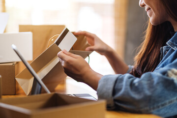 Closeup image of a young woman using tablet pc and credit card for online shopping , opening shopping bags and postal parcel box on the table