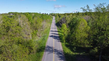 Aerial View of a Countryside Road in Canada with lush greenery and thick tree landscape during blue sky in the summer