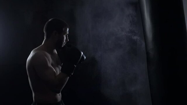 Fighter Practicing Some Kicks With Punching Bag. Kick, punching bag on dark background. Black punching bag weighs at the gym