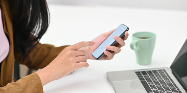 Cropped image of woman holding a white empty screen smartphone in her hands. Woman using mobile with empty screen during work concept.