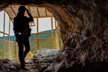 Silhouette of woman with flashlight goes through the entrance of a cave at the Sandia Man Cave, located outside Placitas, New Mexico, with Sandia Mountain forest in the background. 