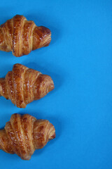 three croissants isolated on blue background flat lay