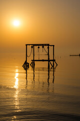 Fisherman wooden structure in the calm water waves at beautiful calm colorful sunset over ocean in morning sky background, Bahrain.