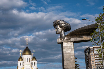 Monument to the revolutionary Olga Genkina and the dome of the Orthodox Church on the forecourt in Ivanovo, Russia. - obrazy, fototapety, plakaty
