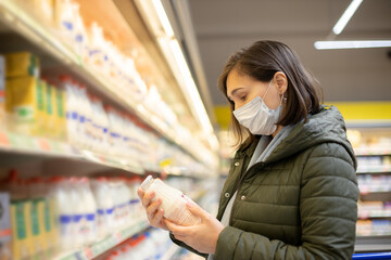 A masked woman buys milk in a supermarket. Shopping for panic during the coonid-19 Coronavirus pandemic. A budget purchase at a supply store.