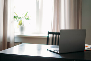 Opened laptop notebook on black table with mobile phone and notes against window at the home