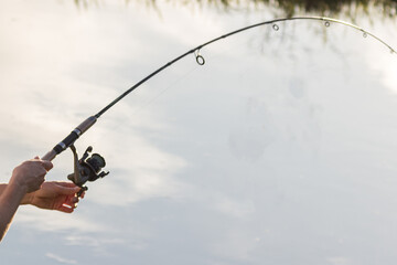 Fishing rod in the hands of a fisherman on the river. beautiful hands with spinning on the background of water. concept for fisherman's day and summer fishing. hobby