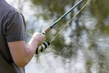 Fishing rod in the hands of a fisherman on the lake. beautiful hands with spinning on the background of water. concept for fisherman's day and summer fishing. hobby