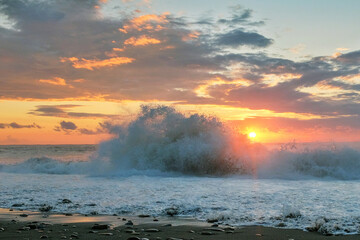 View of the black sea waves splashing on the coast with sunset cloudy sky background