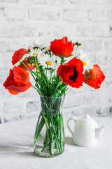 Bouquet of poppies and daisies on the table in a bright room. Home interior beauty comfort concept