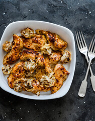 Roasted chicken breast fillets with cauliflower cabbage on a dark background, top view. Delicious lunch, tapas, appetizers