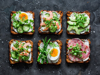 Variety breakfast, appetizer, tapas  sandwiches with cream cheese, egg, asparagus, avocado, cucumber, shrimp, salami, micro greens on a dark background, top view