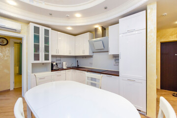 Kitchen area in the hall. Oval white table and chairs. White modern kitchen with built-in...