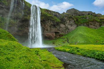 Panoramic view of valley and waterfall Seljalandsfoss in Iceland Many tourists follow the path to see the back of the waterfall. In the summer, there are yellow grass and wildflowers.