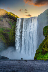Two male and female tourists walking and watching the amazing waterfalls of Skogafoss in southern...
