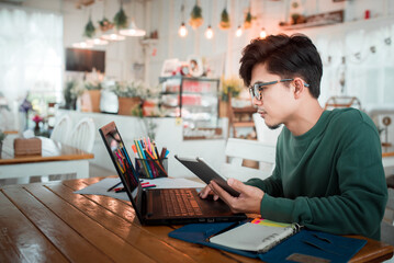 An Asian male student works on a computer touchpad in a coffee shop. A handsome businessman using a laptop sitting at a wooden table in a modern coffee shop, a freelance translator working on a laptop