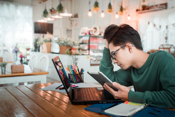 Asian male students feel tired from working with computers. A young businessman uses a laptop to sit at the wooden table of a modern coffee shop. Freelance Translator Working With A Laptop