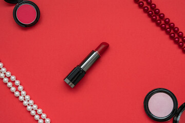 Red lipstick, white and red beads, red and pink eye shadows on a red background