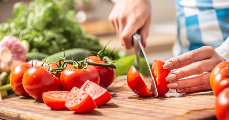 Detail of a tomato freshly cut into halves on a cutting board with cucumber, garlic and more tomatoes aside