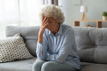 Sad elderly woman cover face with hand sit on couch lost in sad thoughts feeling miserable and lonely, dementia senile diseases, chronic migraine, unhappy unhealthy old person, life or health troubles