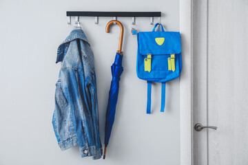 Umbrella with clothes and school backpack hanging on wall in hall - Powered by Adobe