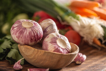 Garlic heads in wooden bowl surrounded by vegetables