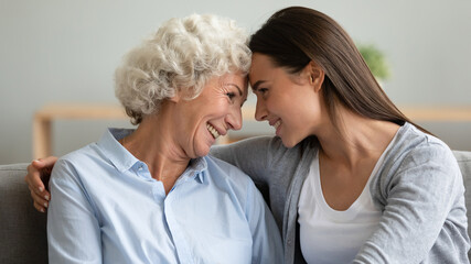 Close up profile faces multi-generational women sit on sofa adult granddaughter and elderly grandmother hugging touch foreheads looking each other smiling enjoy time talk together showing love concept
