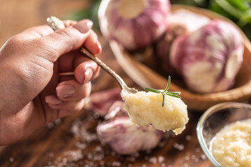 Detail of a teaspoon of garlic paste with fresh garlic in the background