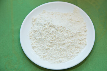 Wheat flour in a plate on green background . The flour is green background on the white plate .