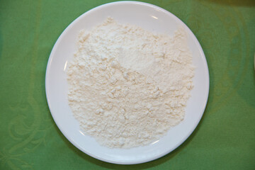Wheat flour in a plate on green background . The flour is green background on the white plate .