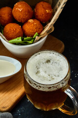 Fresh beer in a glass with cheese croquettes with sauce on a dark background.
