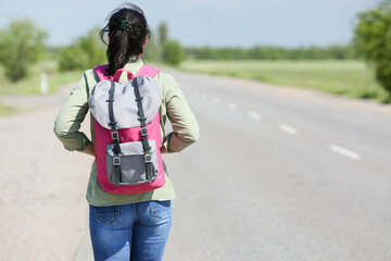 Female traveler with backpack walking along the road