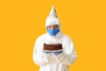 Asian man in biohazard suit and with Birthday cake on color background. Concept of epidemic