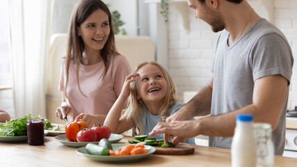 Happy young family with little daughter have fun cooking together in modern kitchen on weekend, smiling parents prepare healthy organic salad, serve breakfast enjoy weekend with small girl child