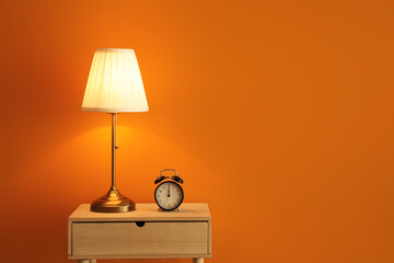 Lamp and alarm clock on table near color wall