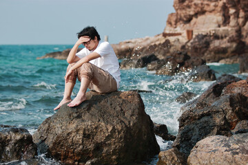 Fototapeta na wymiar Depressed stressed young Aisn man sitting at seashore and feeling disappointment.