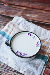 metal Cup with milk and small purple flowers lilac on cotton towel on a wooden table, matte natural still life